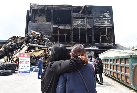 지난 12일 경기 이천시 모가면에 소재한 화재현장에서 유가족들이 검게 타버린 현장을 바라보고 있다. 이미지 제공 : 뉴시스